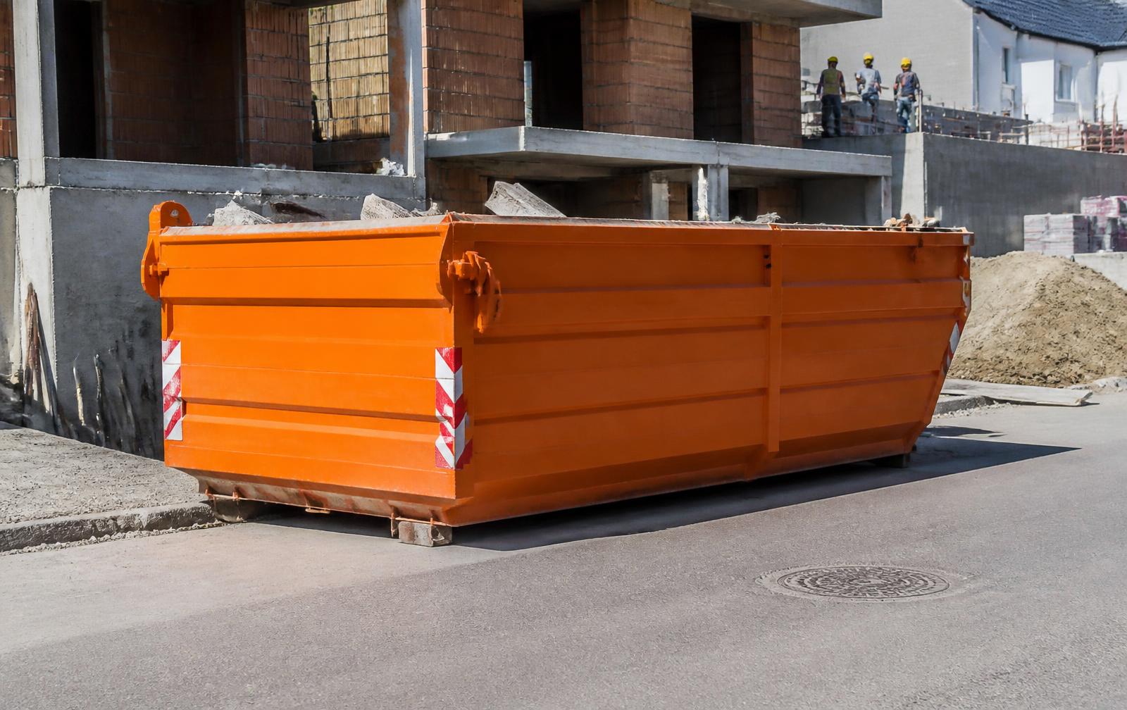 Caçamba de entulho laranja estacionada em frente a uma obra de construção civil
